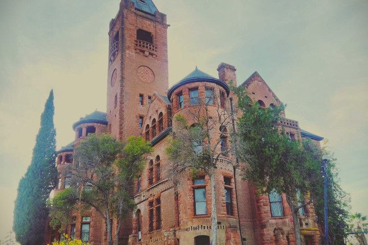 A large, historic red-brick building with towers, surrounded by trees.