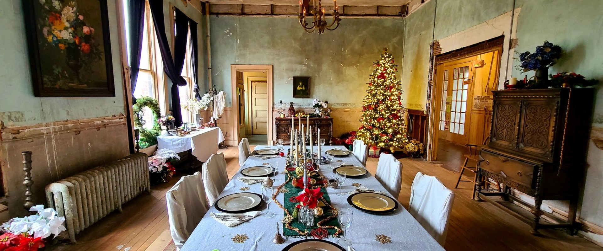 Festive dining room with decorated table and Christmas tree by the window.