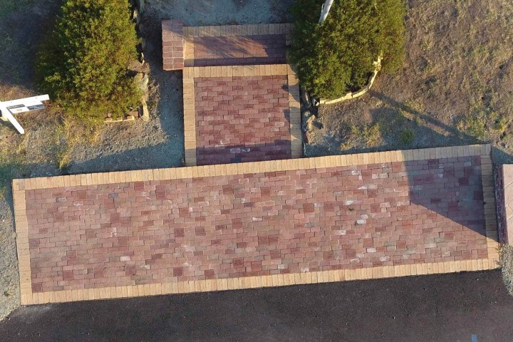 Aerial view of brick pathway with two bushes on a grassy area.