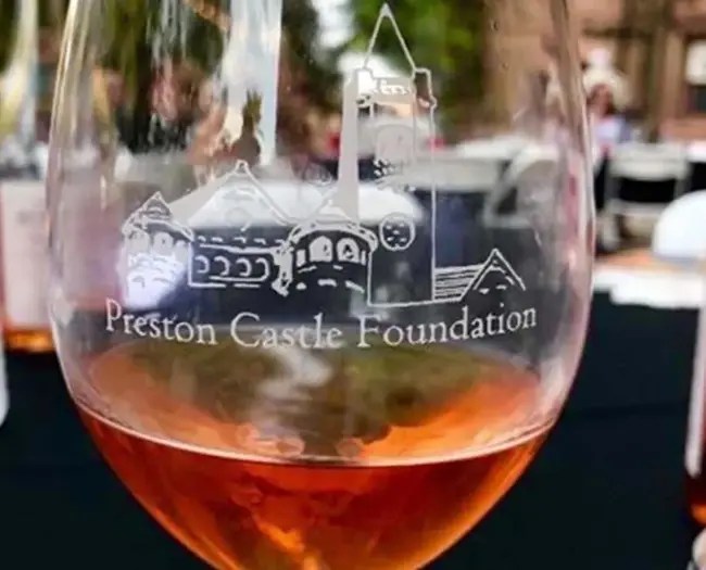 Wine glass with 'Preston Castle Foundation' inscription, rose wine inside, blurred background.